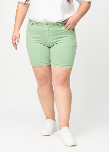 Lysegrønne skinny short shorts, modellnavn Mints, som sitter tett på og slutter midt på låret på en plus-size-modell, sett forfra.
