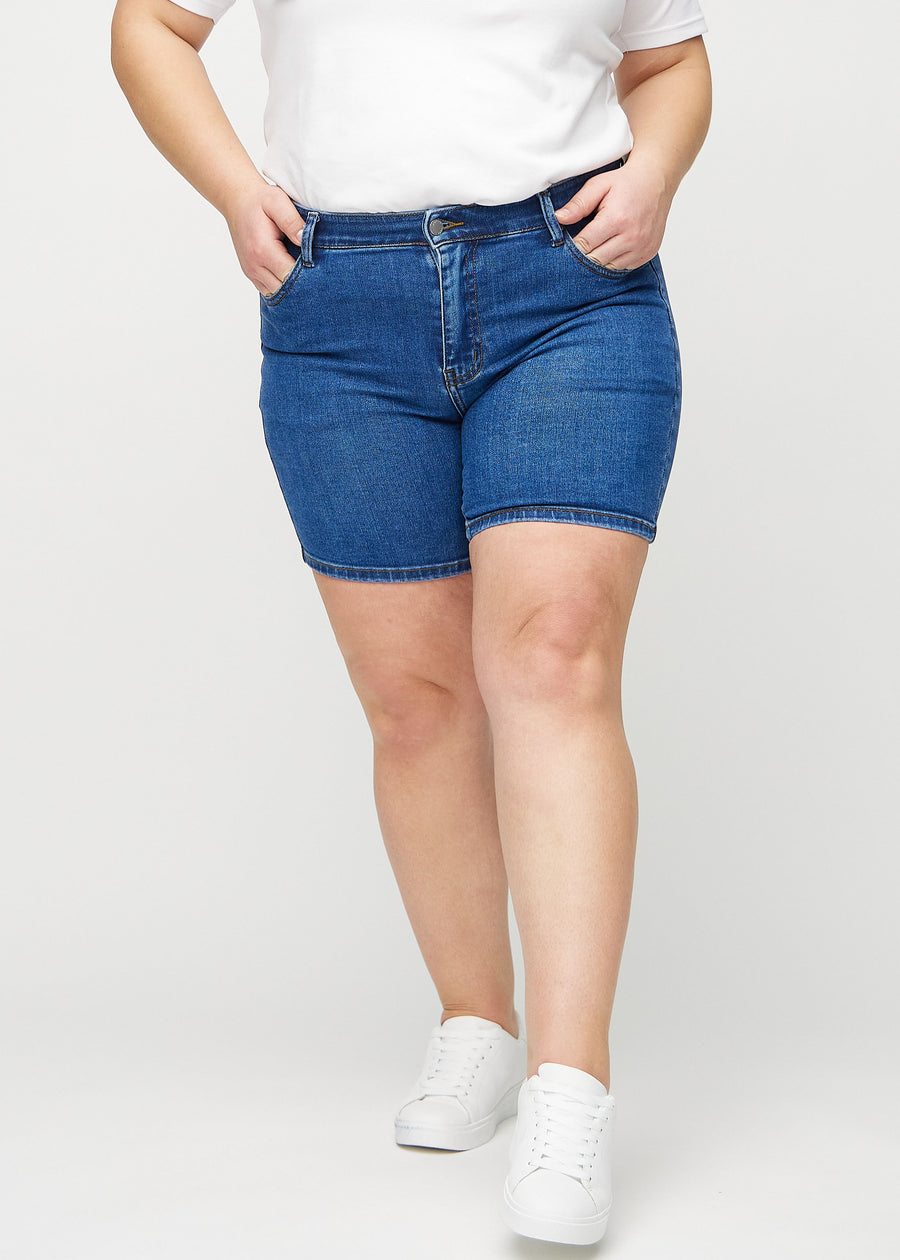 Mørk denim skinny short shorts, modellnavn Oceans, som sitter tett og slutter midt på låret på en plus-size-modell, sett forfra.