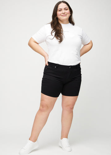 Fullt bilde av en plus-size-modell i svarte skinny short shorts.