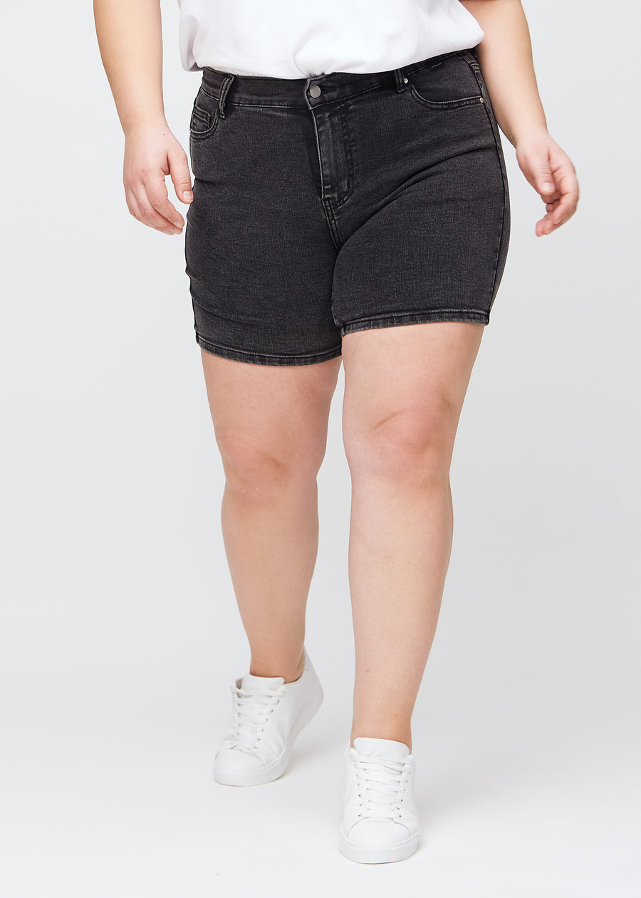 Mørkegrå denim skinny short shorts, modellnavn Shadows, som sitter tett og slutter midt på låret på en plus-size-modell, sett forfra.