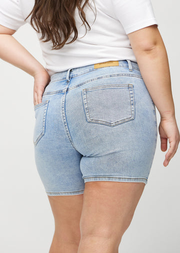 Lys denim skinny short shorts sett bakfra på nært hold på en plus-size modell for å vise detaljer.