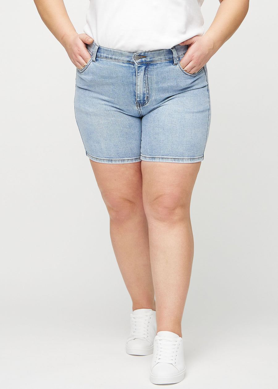 Lys denim skinny short shorts, modellnavn Waves, som sitter tett, og slutter midt på låret på en plus-size modell, sett forfra.