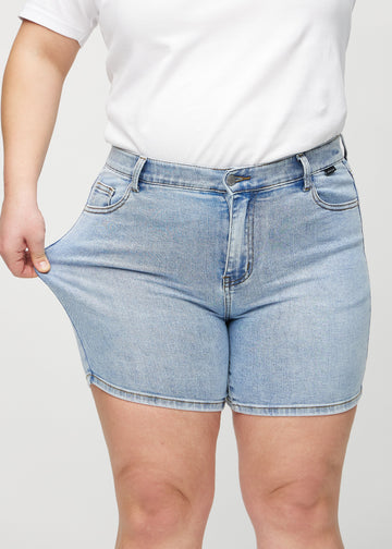 Plus-size modell strekker shortsen ved låret for å vise stretch.