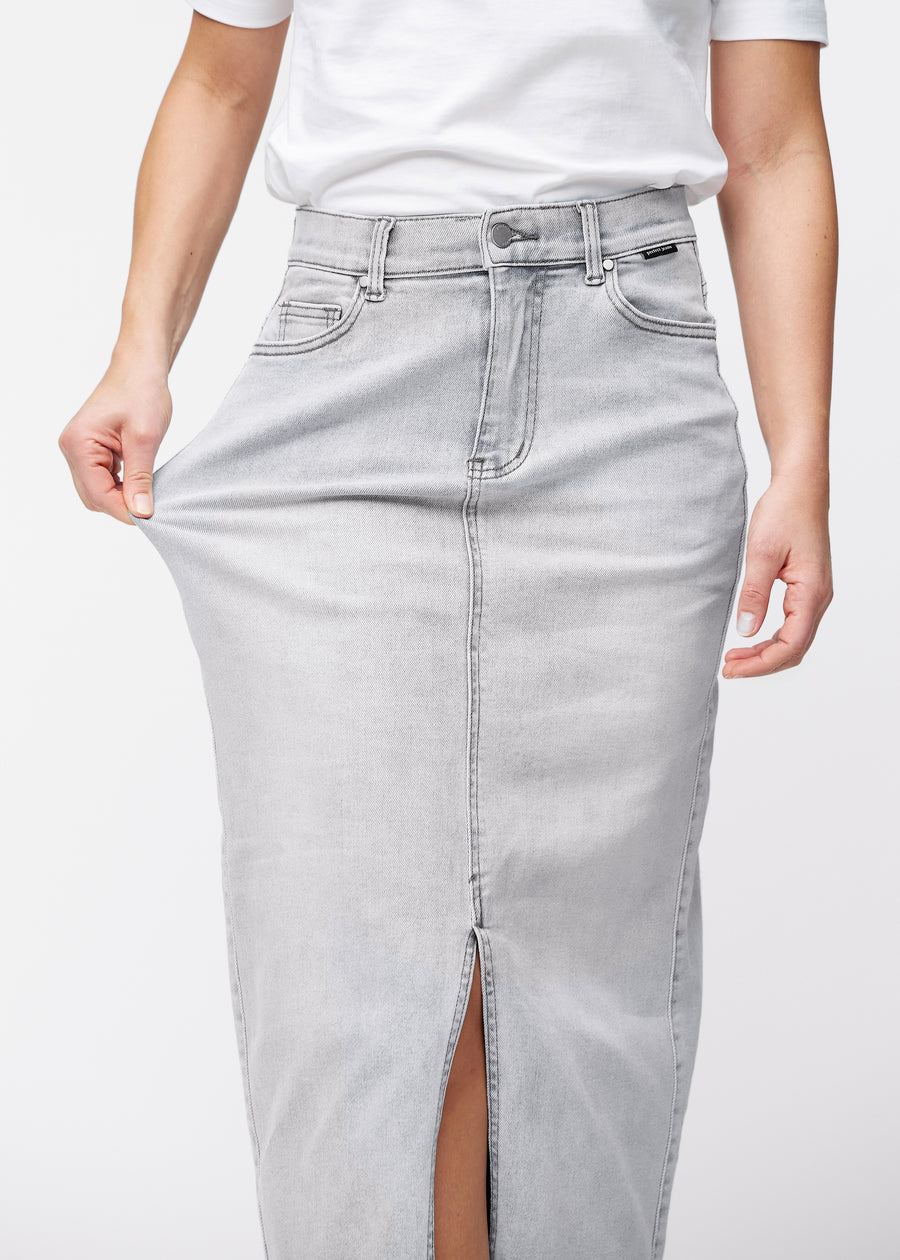 Langt lysegrått denimskjørt til kvinner i fargen Ashes. En modell strekker stoffet ved hoften for å vise stretchen.