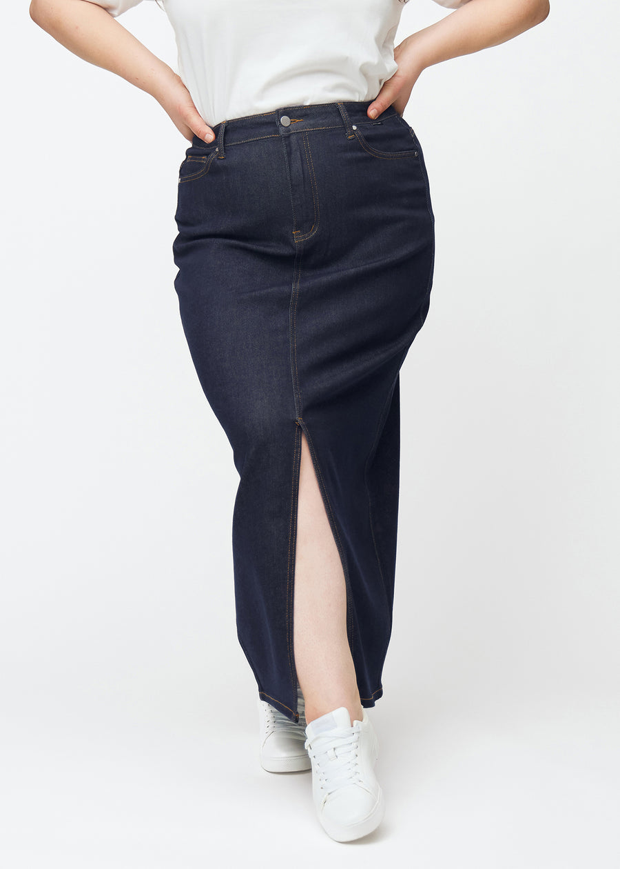 Langt dyp mørkeblått denimskjørt til dame i fargen Midnights sett forfra på plus-size modell, med splitt foran som starter rett under kneet.
