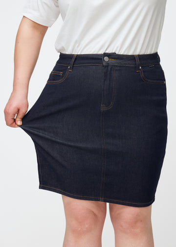 Plus-size modell strekker dyp mørkeblå denimskjørt til dame i fargen Midnights ved låret for å vise stretch.