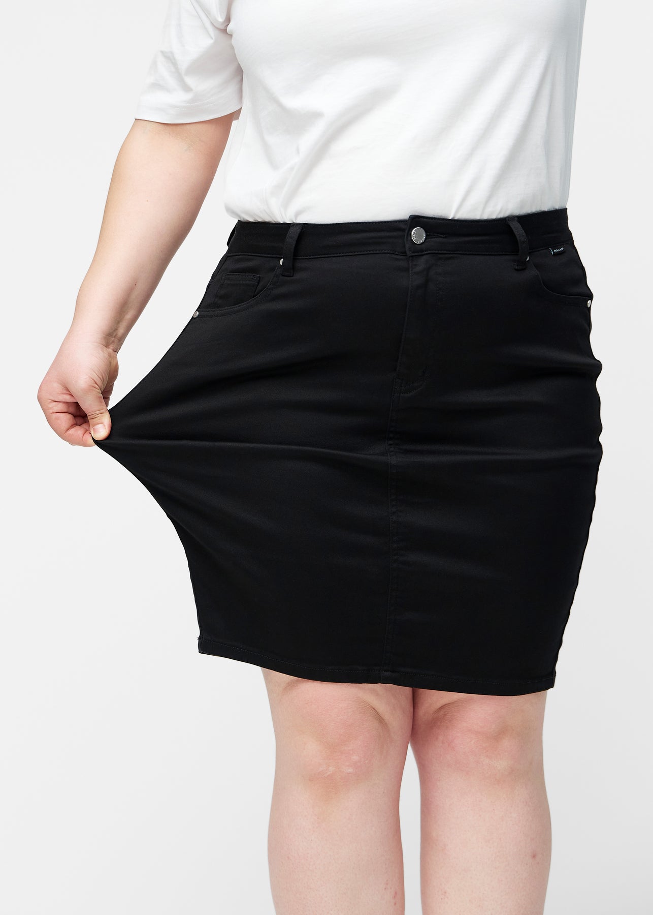 Plus-size model strækker sort, tætsiddende og knælang jeansnederdel ved låret for at vise stretch.