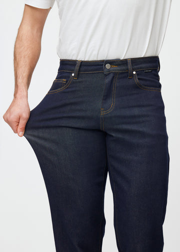 Modell strekker dyp mørkeblå denim jeans til menn i fargen Midnights ved låret for å vise materialets stretch.