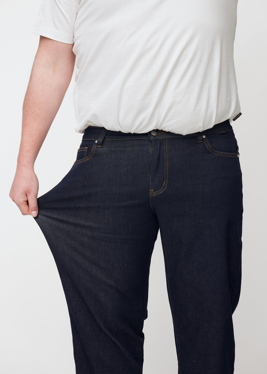 Plus-size-modell strekker dyp mørkeblå denim jeans til menn i fargen Midnights ved låret for å vise materialets stretch.