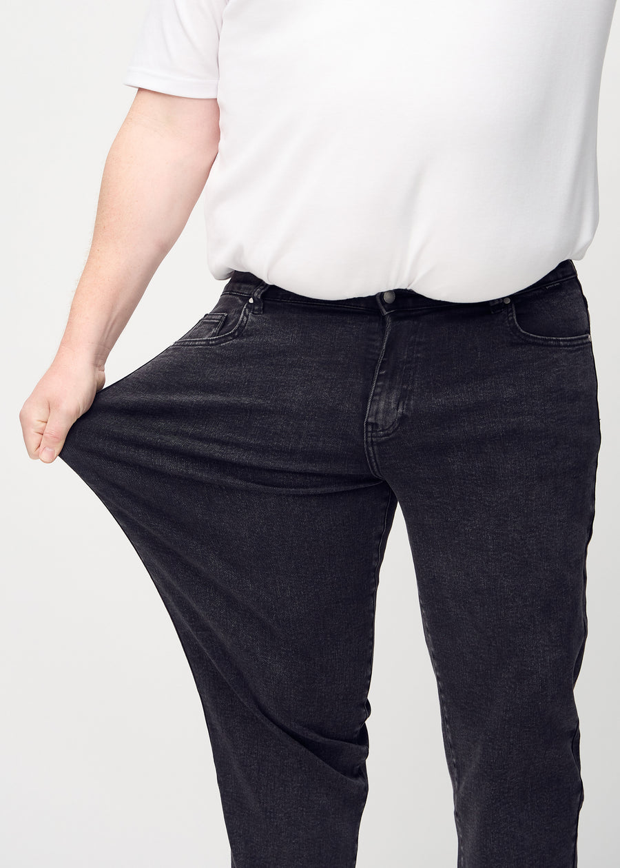 Plus-size-modellen strekker jeansene ved låret for å vise stretch.