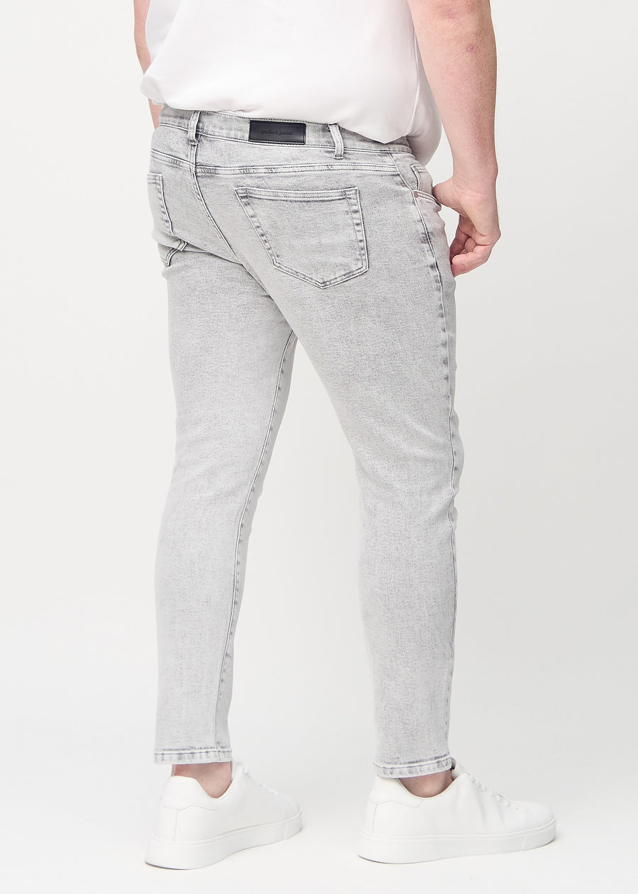 Lysegrå denimjeans i slim fit sett bakfra på en plus-size-modell for å vise hele produktet.