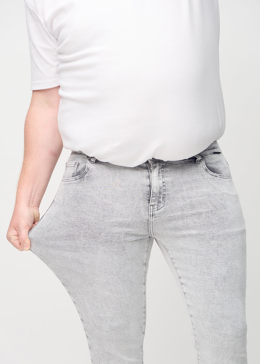 Plus-size-modell strekker jeansene ved låret for å vise materialets stretch.