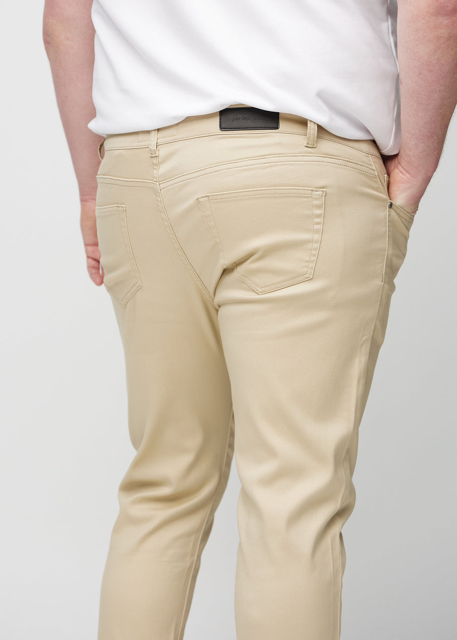 Nærbilde bakfra av beige jeans i slim fit på en plus-size-modell som viser detaljer.