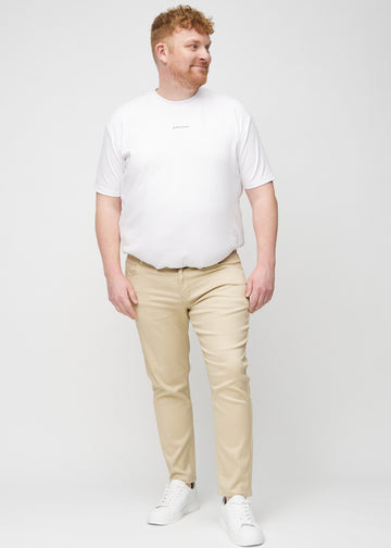 Helbilde av en plus-size-modell i beige jeans i slim fit.