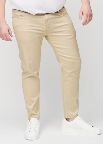 Beige jeans i slim fit, modellnavn Gazelles, som sitter tett langs bena på en plus-size-modell, sett forfra.