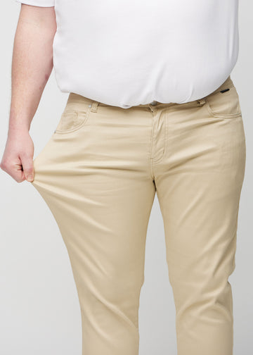 Plus-size-modell strekker jeansene ved låret for å vise materialets stretch.