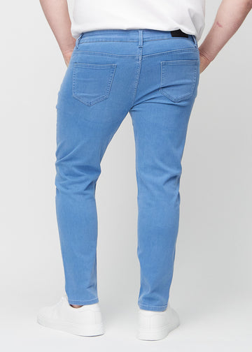 Blå jeans i slim fit sett bakfra på en plus-size-modell for å vise hele produktet.