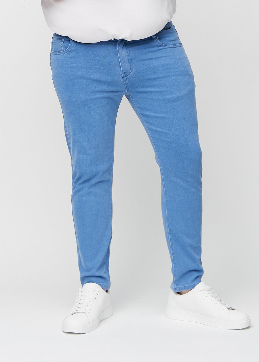 Blå jeans i slim fit, modellnavn Geraniums, som sitter tett langs bena på en plus-size-modell, sett forfra.