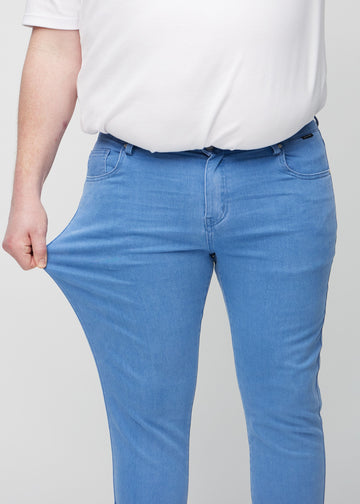 Plus-size-modell strekker jeansene ved låret for å vise materialets stretch.
