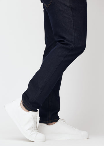 Dyp mørkeblå denim jeans til menn i fargen Midnights med slim passform sett på nært hold ved anklene på plus-size-modell for å vise den smale avslutningen.