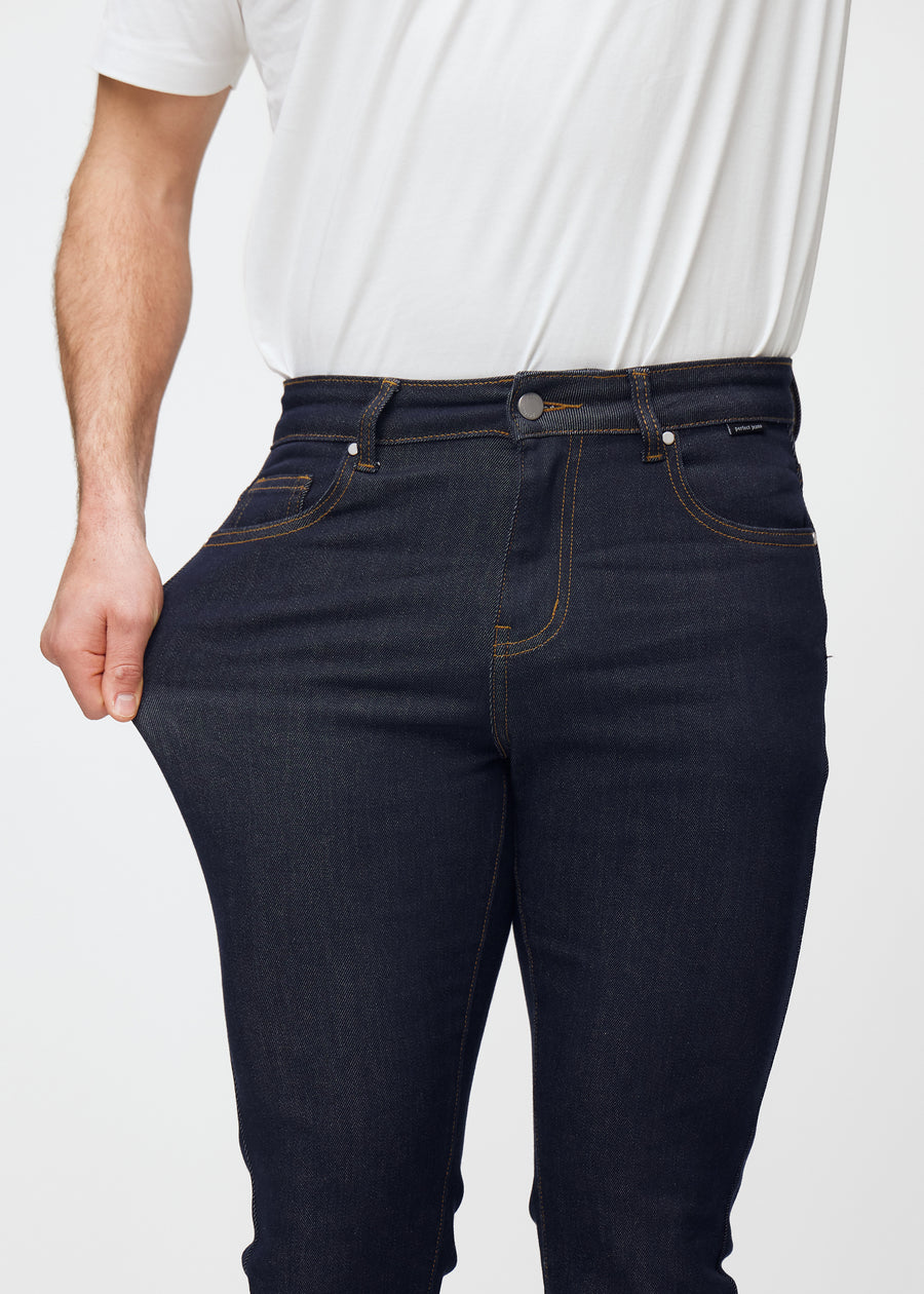 Modell strekker dyp mørkeblå denim jeans til menn i fargen Midnights ved låret for å vise materialets stretch.