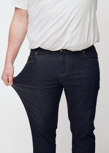 Plus-size-modell strekker dyp mørkeblå denim jeans til menn i fargen Midnights ved låret for å vise materialets stretch.