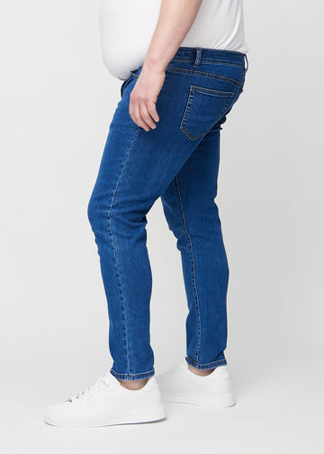 Mørkeblå denimjeans i slim fit sett fra siden på en plus-size-modell.