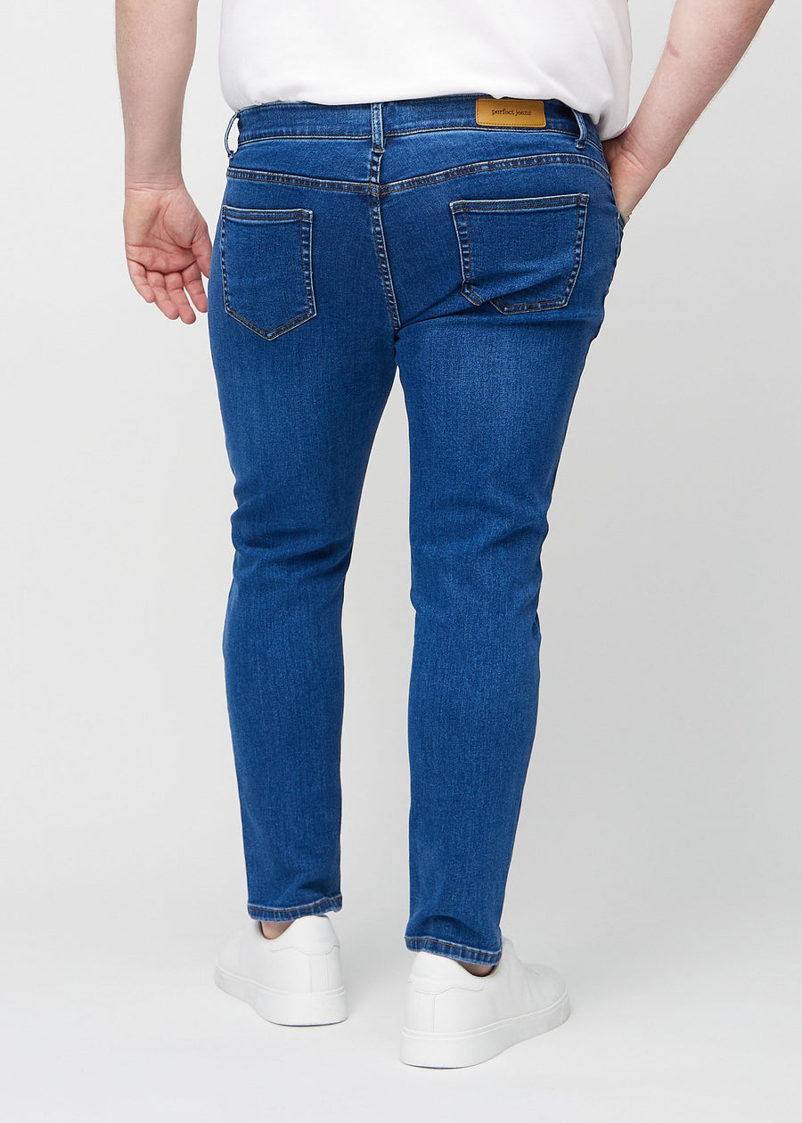Mørkeblå denimjeans i slim fit sett bakfra på en plus-size-modell for å vise hele produktet.