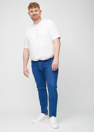 Helbilde av en plus-size-modell i mørkeblå denimjeans i slim fit.