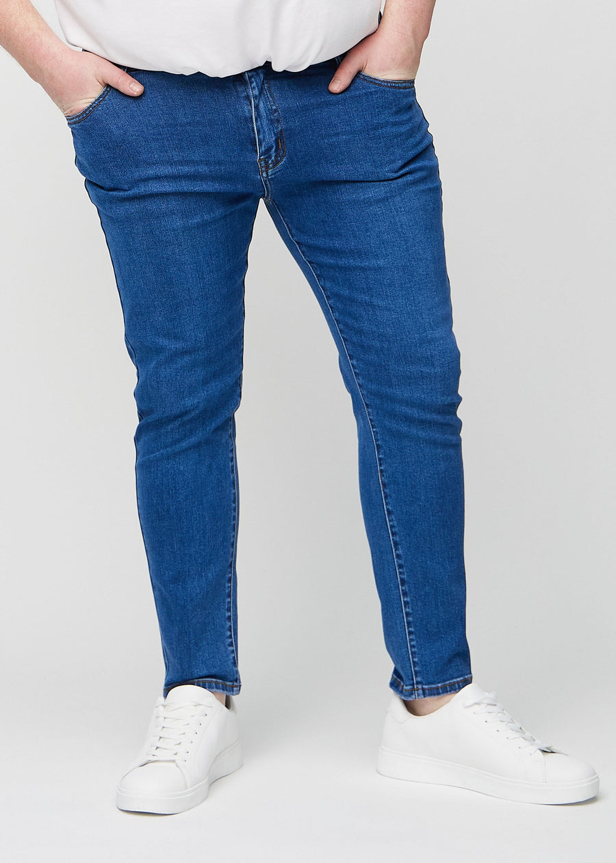 Mørkeblå denimjeans i slim fit, modellnavn Oceans, som sitter tett langs bena på en plus-size-modell, sett forfra.