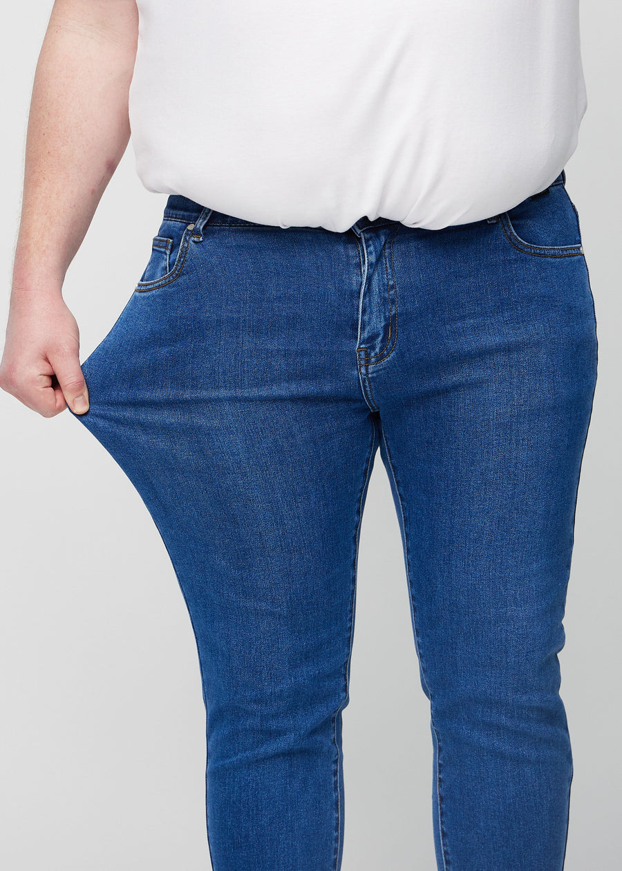 Plus-size-modell strekker jeansene ved låret for å vise materialets stretch.