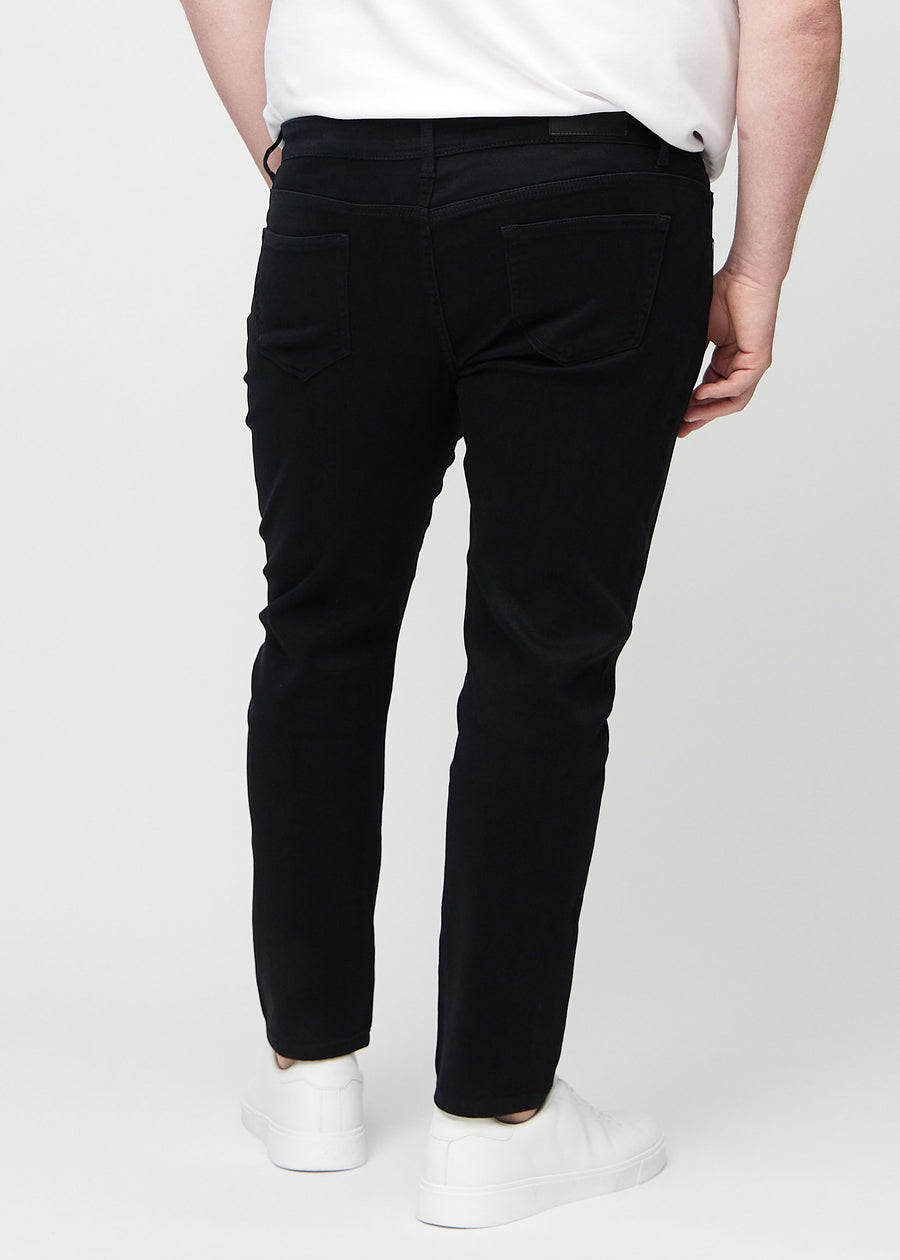 Svarte jeans i slim fit sett bakfra på en plus-size-modell for å vise hele produktet.