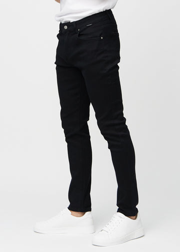 Svarte jeans i slim fit sett fra siden på en modell.