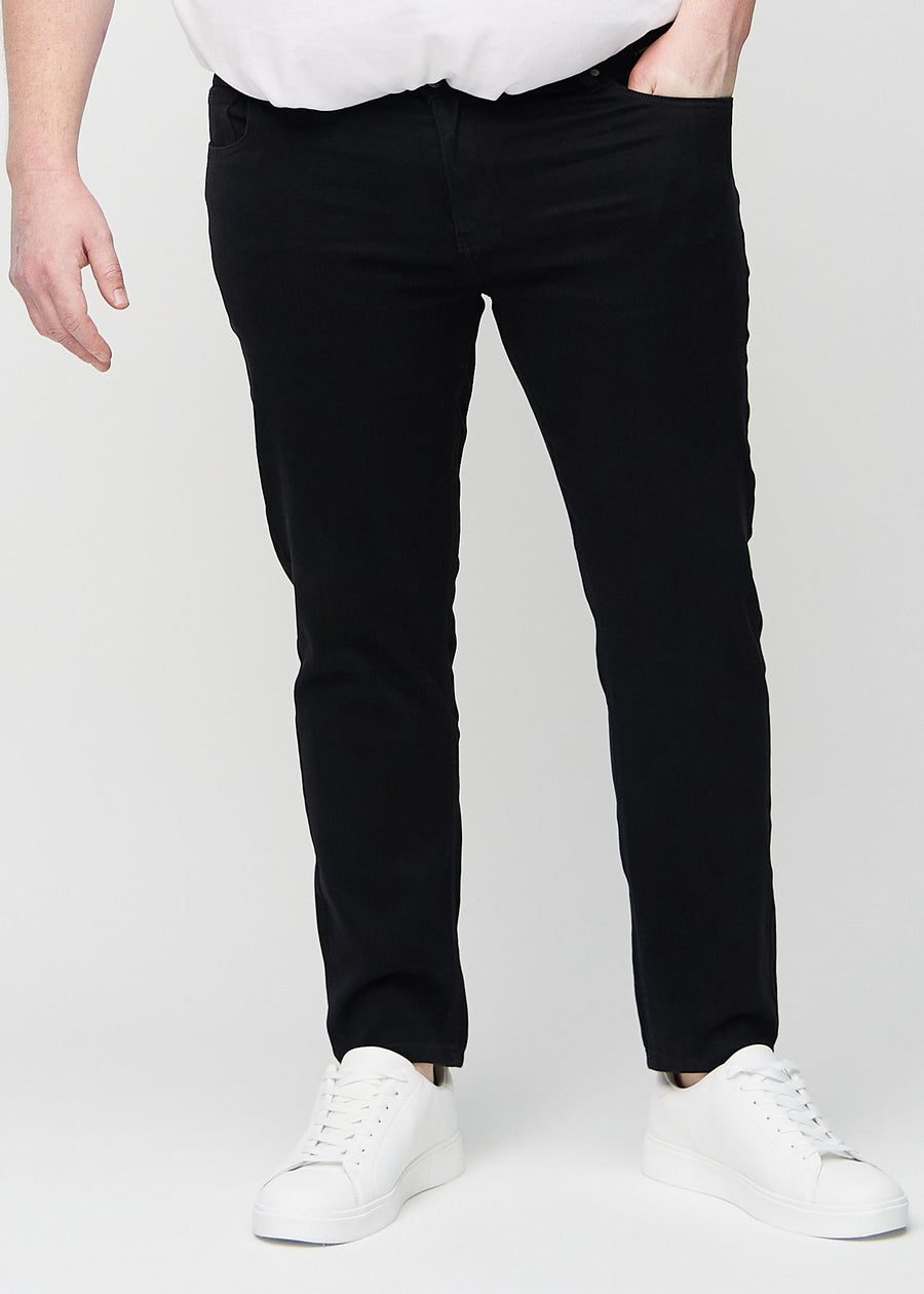 Svarte jeans i slim fit, modellnavn Ravens, som sitter tett langs bena på en plus-size-modell, sett forfra.