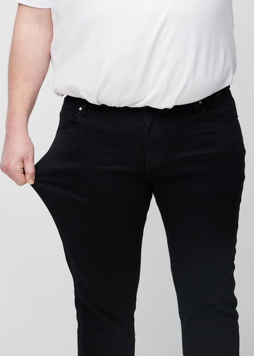 Plus-size-modell strekker jeansene ved låret for å vise materialets stretch.