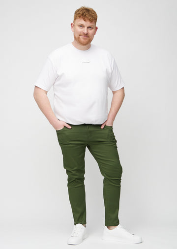 Helbilde av en plus-size-modell i mørkegrønne jeans i slim fit.
