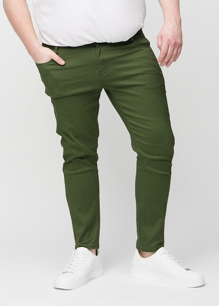 Mørkegrønne jeans i slim fit, modellnavn Renewals, som sitter tett langs bena på en plus-size-modell, sett forfra.
