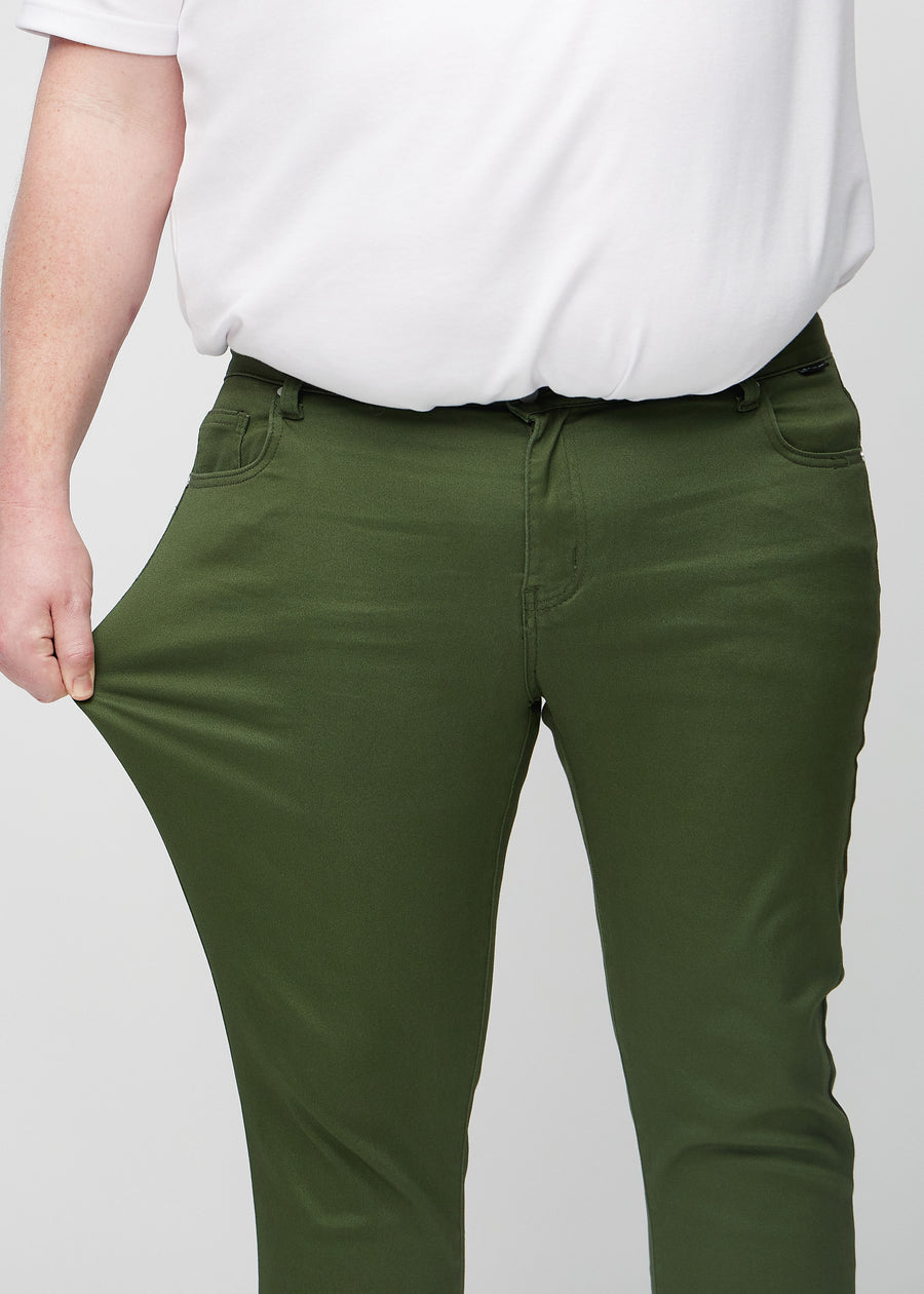 Plus-size-modell strekker jeansene ved låret for å vise materialets stretch.