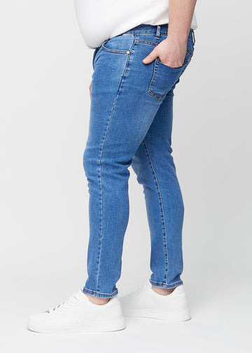 Blå denimjeans i slim fit sett fra siden på en plus-size-modell.