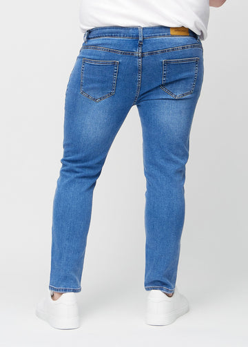 Blå denimjeans i slim fit sett bakfra på en plus-size-modell for å vise hele produktet.