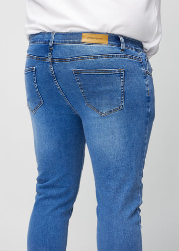 Nærbilde bakfra av blå denimjeans i slim fit på en plus-size-modell som viser detaljer.