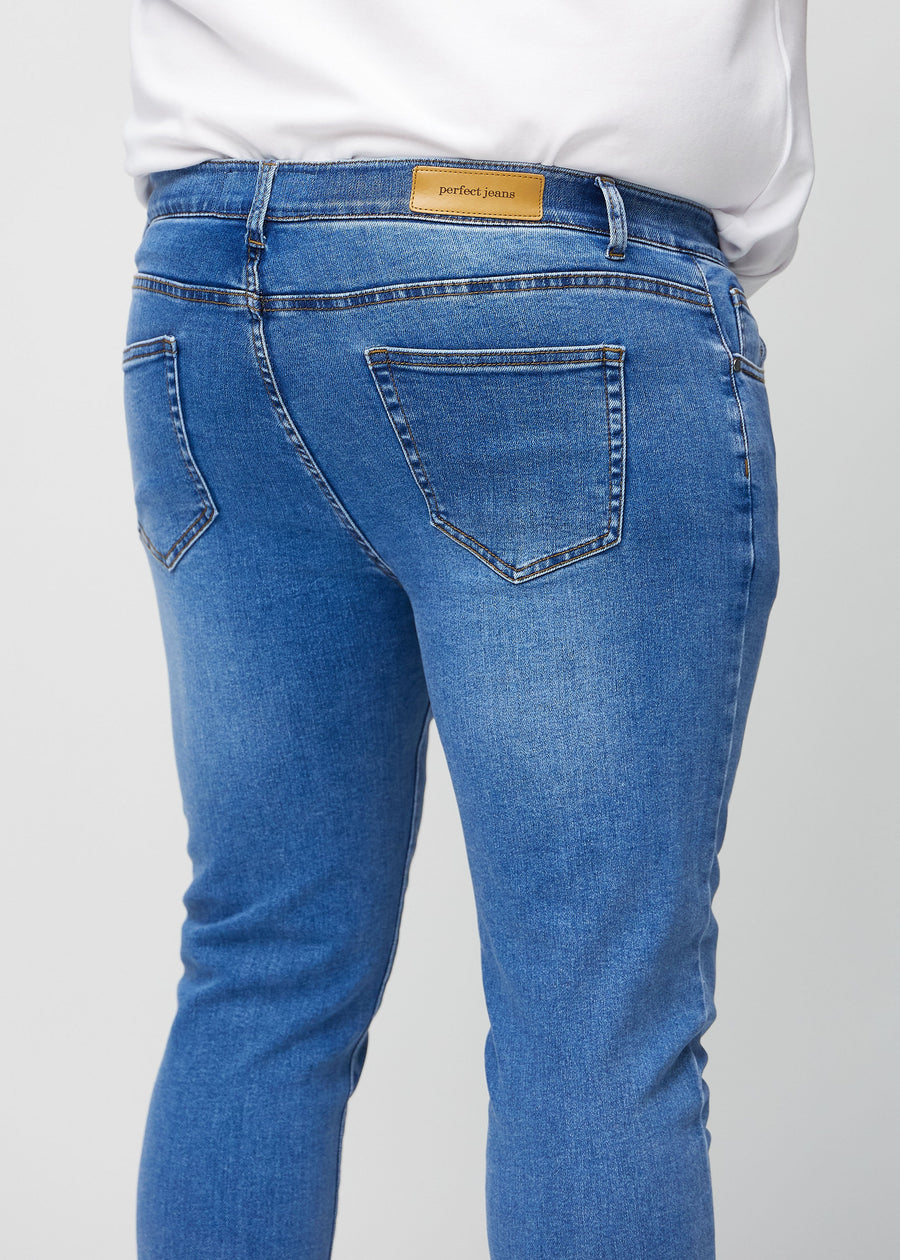Nærbilde bakfra av blå denimjeans i slim fit på en plus-size-modell som viser detaljer.