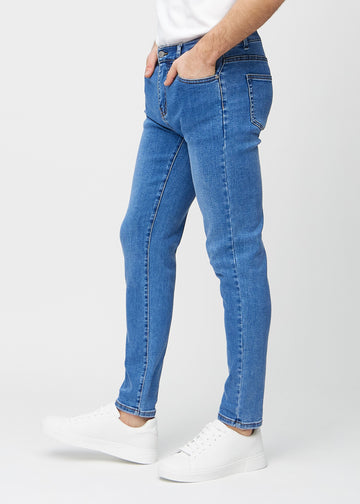 Blå denimjeans i slim fit sett fra siden på en modell.