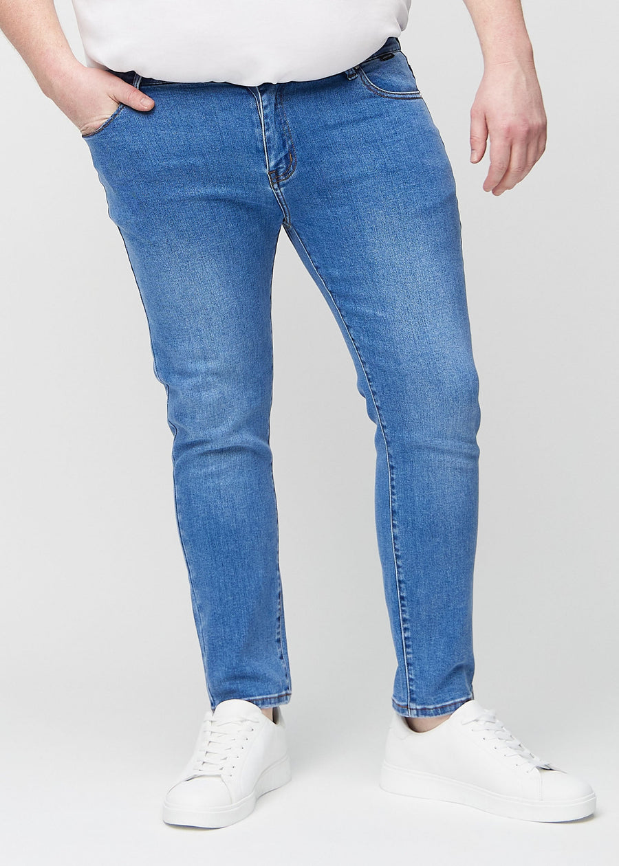Blå denimjeans i slim fit, modellnavn Rivers, som sitter tett langs bena på en plus-size-modell, sett forfra.