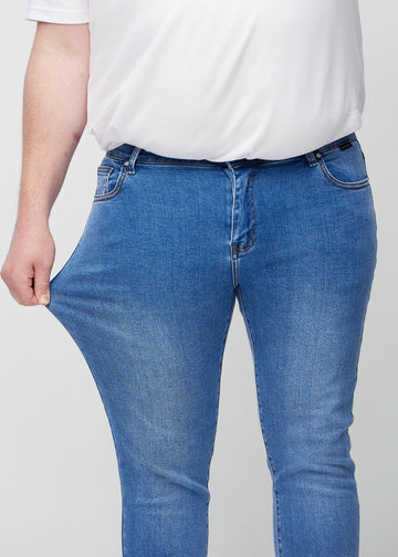 Plus-size-modell strekker jeansene ved låret for å vise materialets stretch.