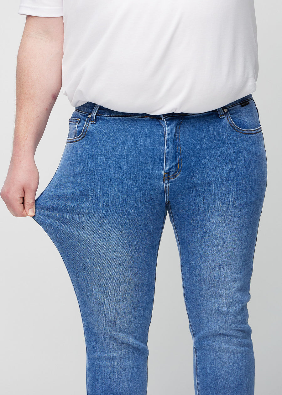 Plus-size-modell strekker jeansene ved låret for å vise materialets stretch.