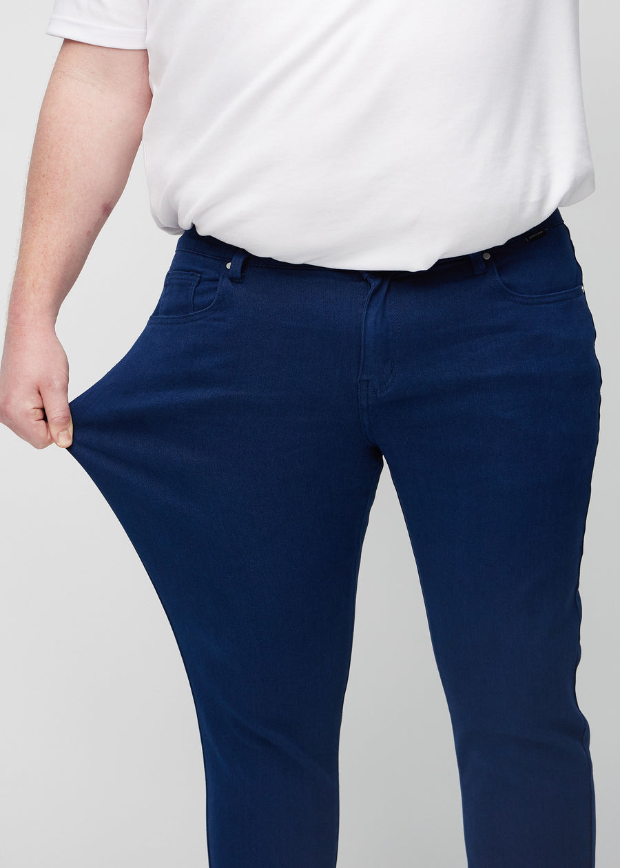 Plus-size-modell strekker jeansene ved låret for å vise materialets stretch.