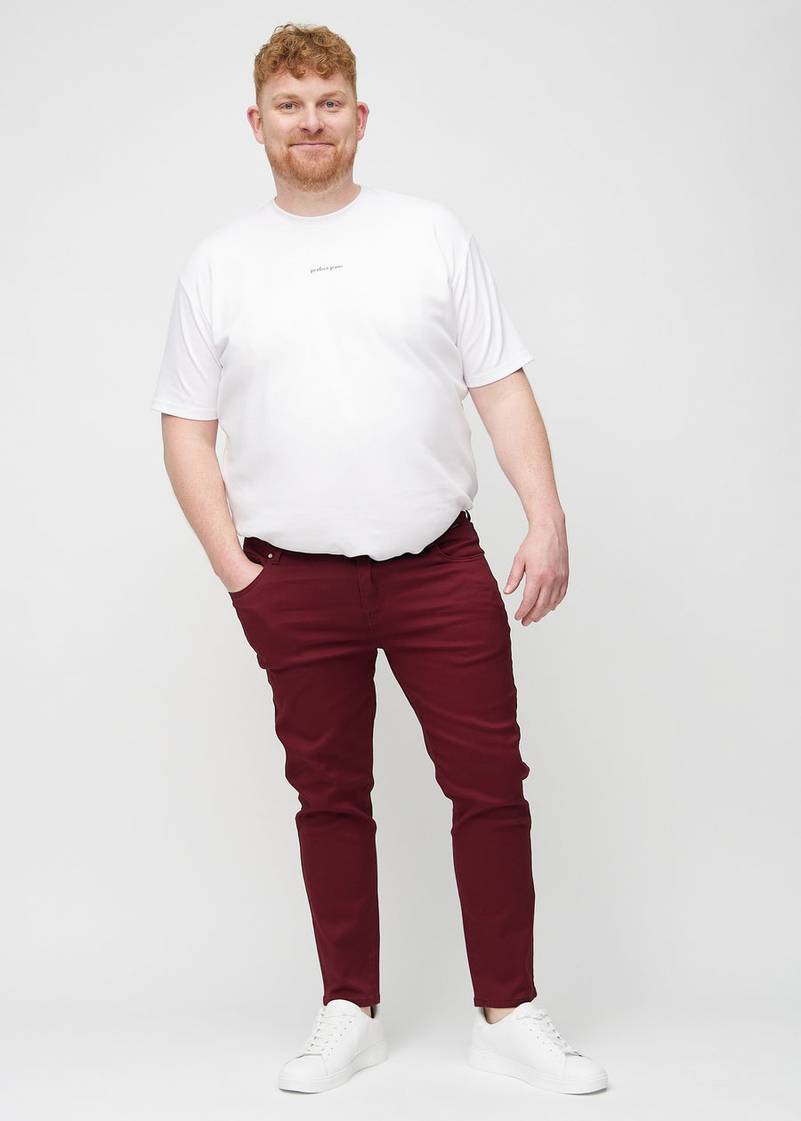 Helbilde av en plus-size-modell i mørkerøde jeans i slim fit.