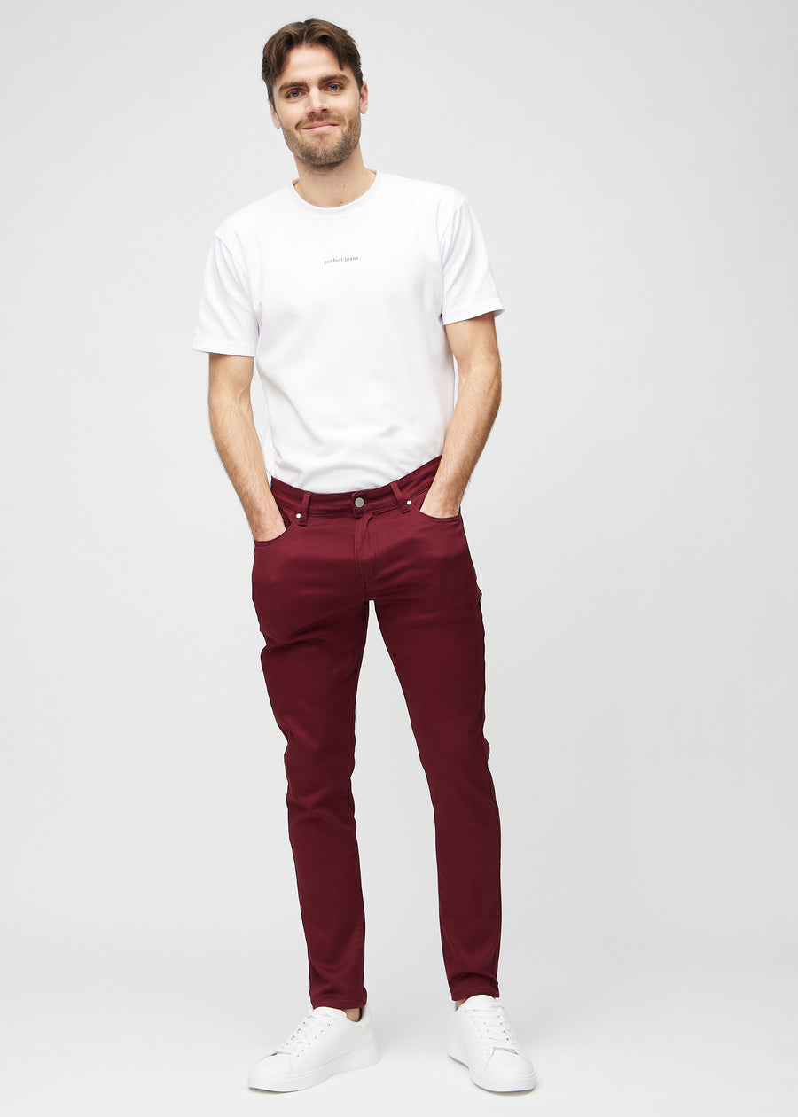 Helbilde av en modell i mørkerøde jeans i slim fit.