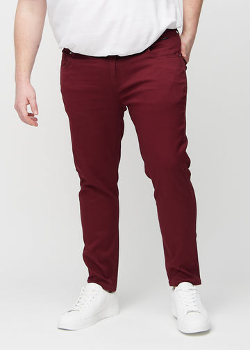 Mørkerøde jeans i slim fit, modellnavn Santas, som sitter tett langs bena på en plus-size-modell, sett forfra.